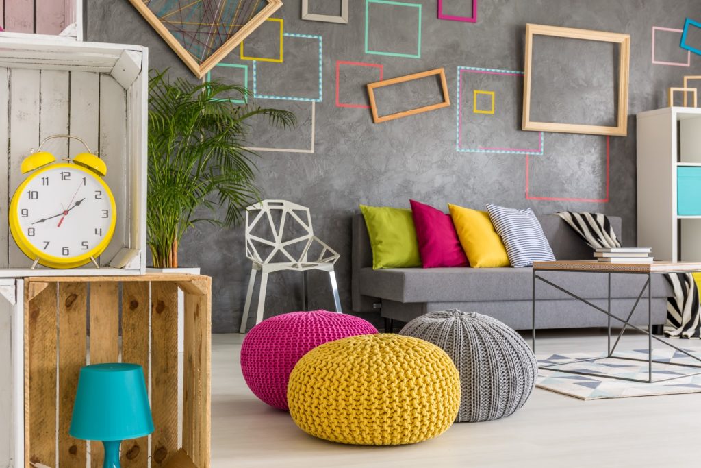 Modern home decor in a living room featuring a gray sofa with colorful pillows, unique geometric wall frames, and stylish knitted poufs.